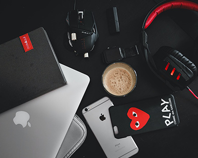 Laptop mit Tasche, Notebook, Uhr, Kopfhörer, Smartphone mit Hülle und eine Tasse Kaffee vor schwarzem Hintergrund.